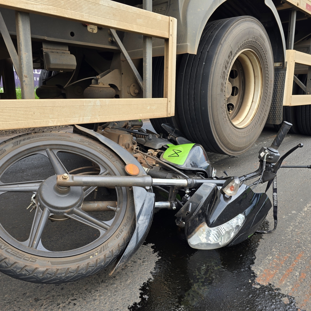 Homem fica debaixo dos rodados de caminhão após moto escorregar em óleo derramado na pista