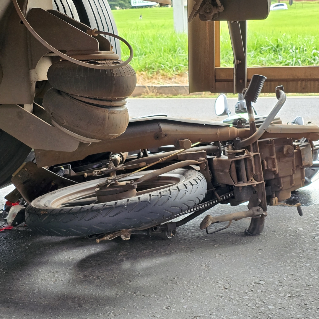 Homem fica debaixo dos rodados de caminhão após moto escorregar em óleo derramado na pista