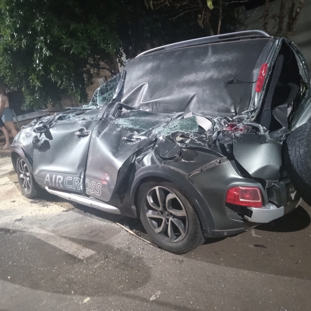 Automóvel fica destruído após carreta tombar e cair sobre automóvel